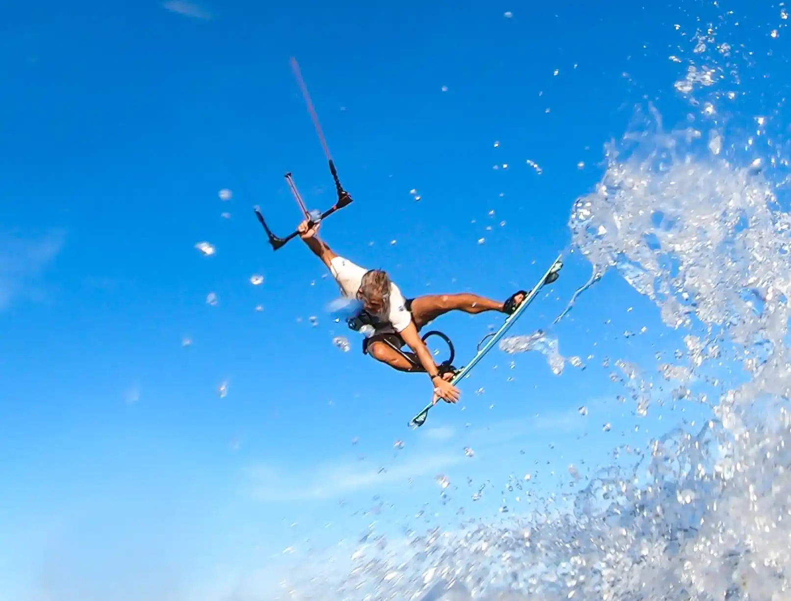 Kitesurfeur en plein saut au-dessus de la gerbe d'eau, ciel bleu